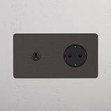 Bronzener und schwarzer Kipphebel & SchuKo-Modul Zweifachrahmen mit Steckdosen, montiert auf einer weißen Wand.