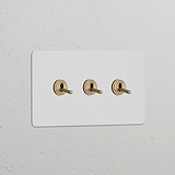 Zweifachrahmen mit 3x Kipphebelschalter in antikem Messing auf lackierbarem weißem Panel an der Wand.