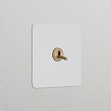 Tastschalter mit Kipphebel in lackierbarem Einfachrahmen, antikes Messing, auf weißer Wand montiert.