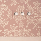 3-fach SchuKo-Steckdoseneinsatz (Typ F) in transparent-weißem Rahmen auf rosa floral gemusterter Wand.