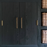 Medium handgreep in Antiek Messing, Sycamore Meubelgreep 224mm, op donkerhouten kast met rieten manden ernaast.