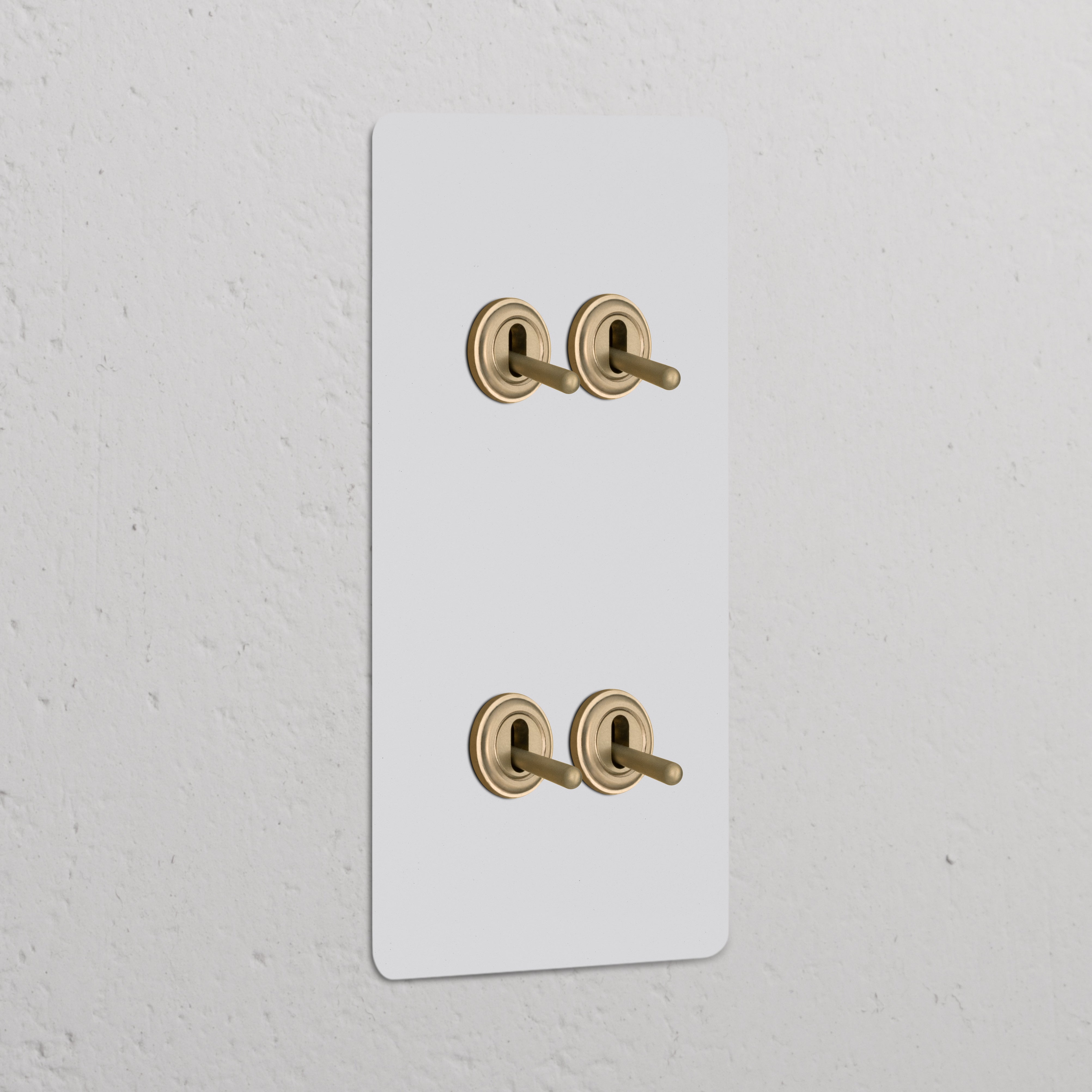 Beschilderbaar Antiek Messing 4x Wissel-Tuimelschakelaar, Dubbele Verticale Afdekplaat op een witte muur.