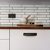 Elm Komgreep 164mm - Brons greep op kastdeur in een keuken met witte tegels en houten aanrechtblad.