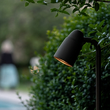 Ealing Pad Spotlight - Brons, close-up tussen groen gebladerte met een warme gloed, waardoor een serene buitensfeer ontstaat.