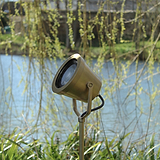 Cambridge Grondschijnwerper in antieke messing geplaatst buiten tussen groene planten bij een meer.