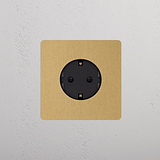 Rond Schuko Type F Stopcontact in antieke messing met zwart inzetstuk, Enkele Afdekplaat tegen een witte muur.