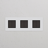 Drievoudige bronzen overschilderbare schakelaar met afdekplaat voor drievoudige schakelaars & dimmers op een gestructureerde muur.