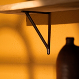 Brixton Plankdrager 150mm - Brons, een bronzen beugel voor planken, gemonteerd op een warmgele muur.