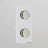 Dubbele verticale dimmers in gepolijst nikkel, op een beschilderde afdekplaat.