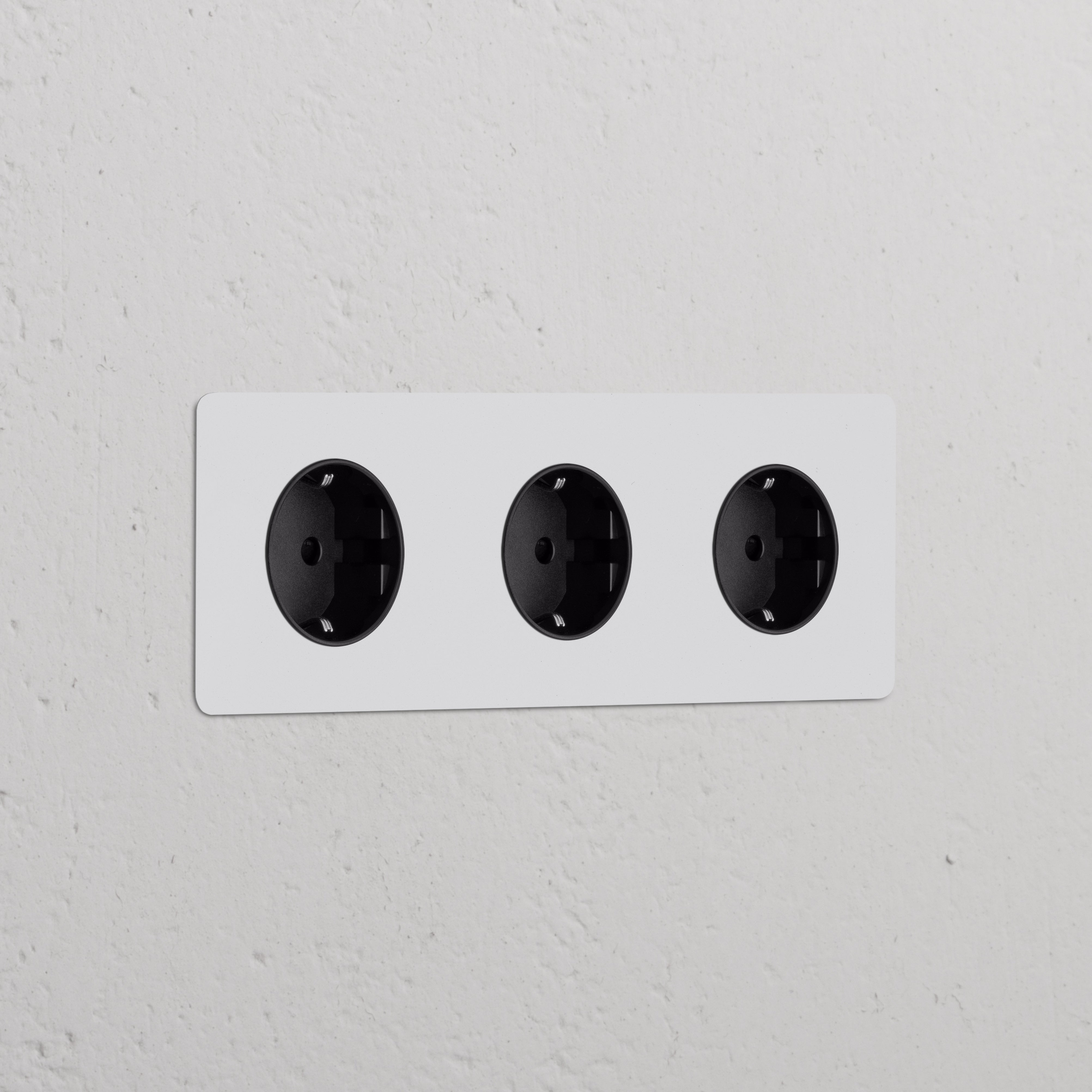 Drievoudig zwart overschilderbare Type F Schuko stopcontacten op witte muur, 3x Rond design met Drievoudige Afdekplaat.