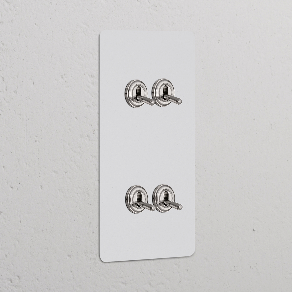 4x Wissel-Tuimelschakelaar (Dubbele Verticale Afdekplaat) in Beschilderbaar Gepolijst Nikkel op een witte muur.