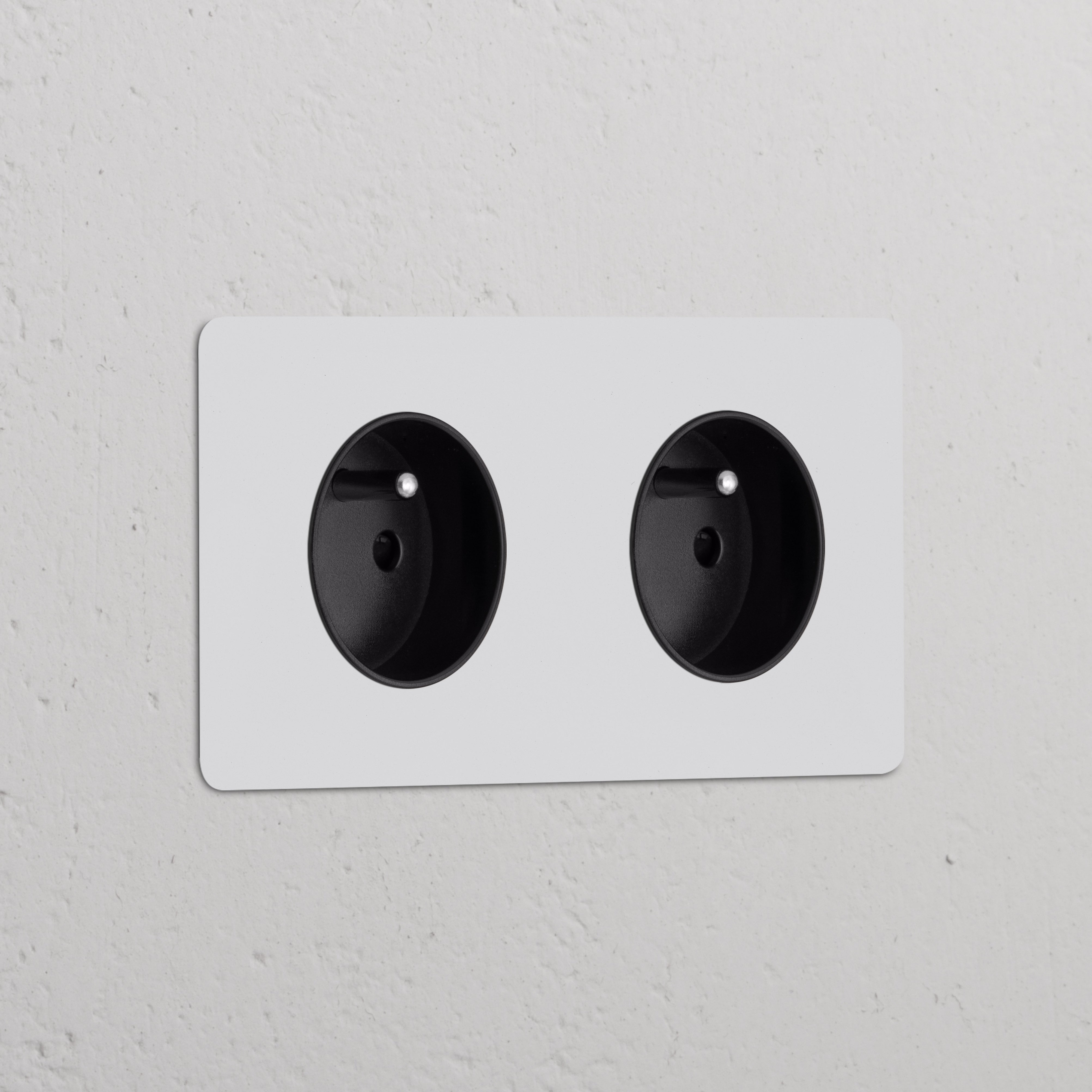 Zwart 2x Rond Belgisch Type E dubbele stopcontacten met beschilderbaar afdekplaat op een witte muur.