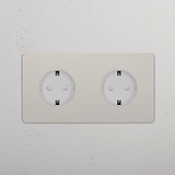 2x Rond Schuko Type F Stopcontact met Dubbele Afdekplaat in gepolijst nikkel en witte inzet op een witte muur.