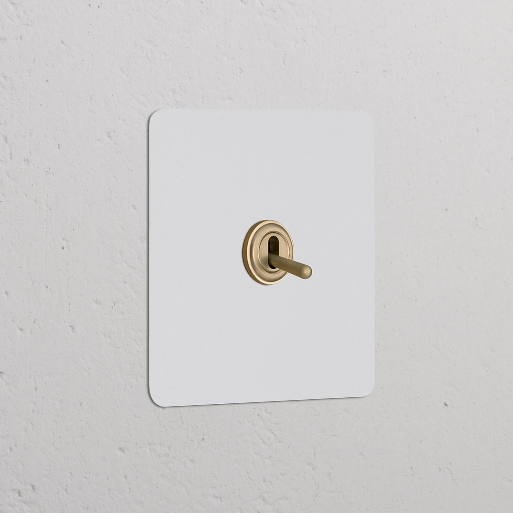 Permutateur à Levier (Plaque Simple) en laiton ancien, interrupteur simple sur mur texturé blanc.