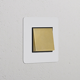 Interrupteur VV Carré (Plaque Simple) en Laiton Ancien avec Insert Noir sur un mur blanc, partiellement recouvert par une note.