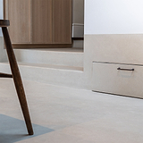 Poignée de Meuble Sycamore 128mm poignée en bronze sur meuble en bois clair, avec un pied de chaise visible au premier plan.