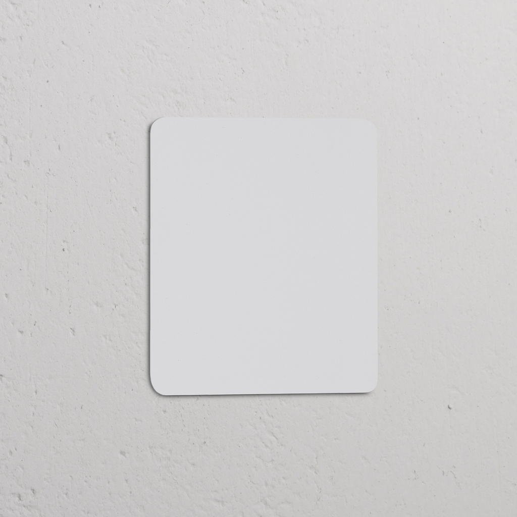 Plaque Obturatrice Simple Peignable blanche pour Prises & Modules Simple, avec coins arrondis sur un mur texturé.
