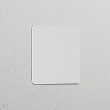 Plaque Obturatrice Simple Peignable blanche pour Prises & Modules Simple, avec coins arrondis sur un mur texturé.
