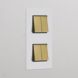 Interrupteur VV Carré x4 Vertical (Plaque Double) en finition laiton avec insert noir sur plaque murale blanche.