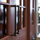 Harper Stoßgriff 1x (320 mm) – Bronzefarbene mittelgroße Türziehgriffe an einer Holztür mit Glasscheiben.