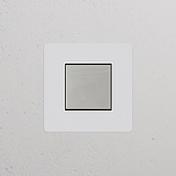 Tastschalter im Einfachrahmen mit zentriertem Wippschalter – lackierbar, poliertes Nickel, weiß an der Wand.