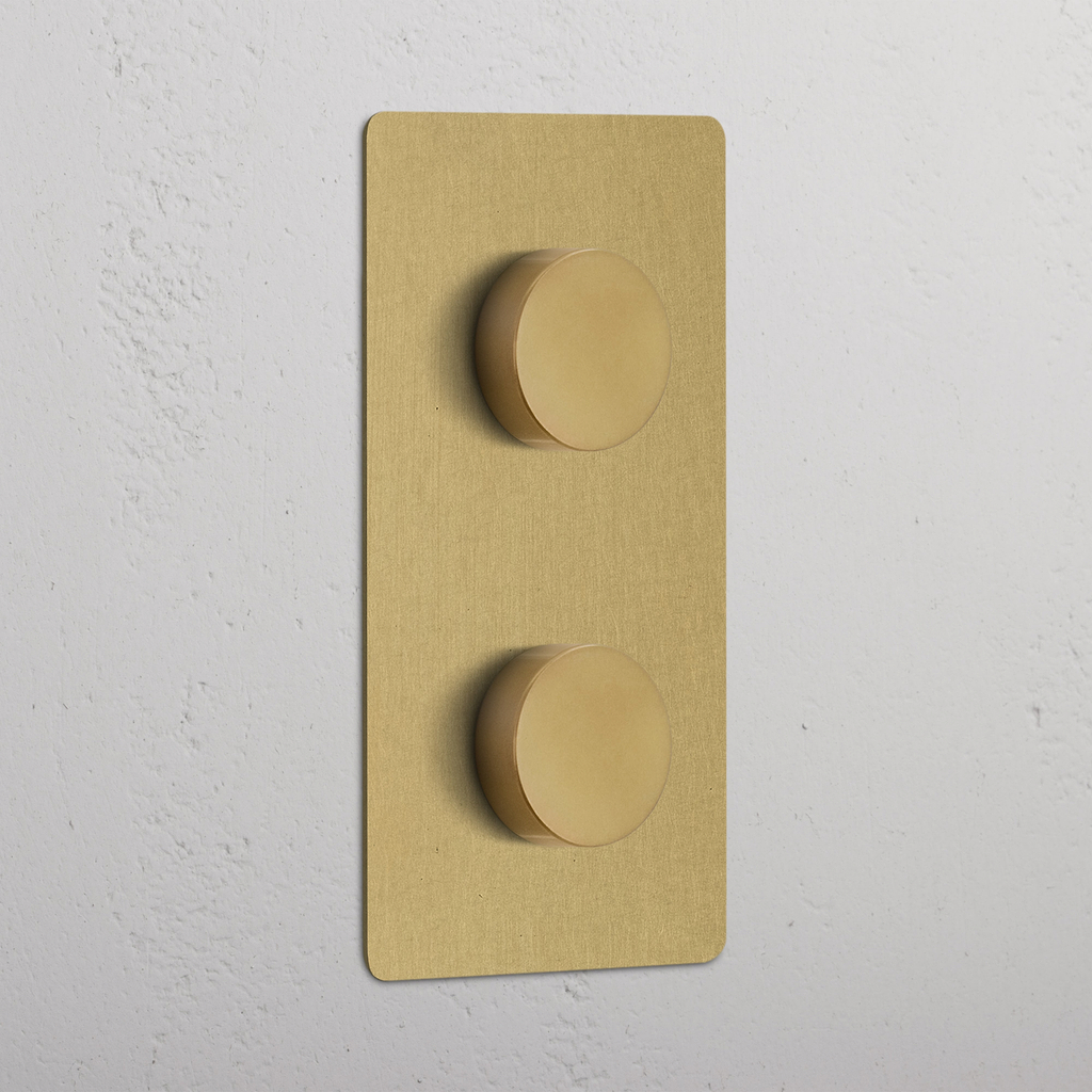Vertikaler Zweifachrahmen mit 2x Mehrpunkt-Dimmerschalter, antikes Messing, an weißer Wand montiert.