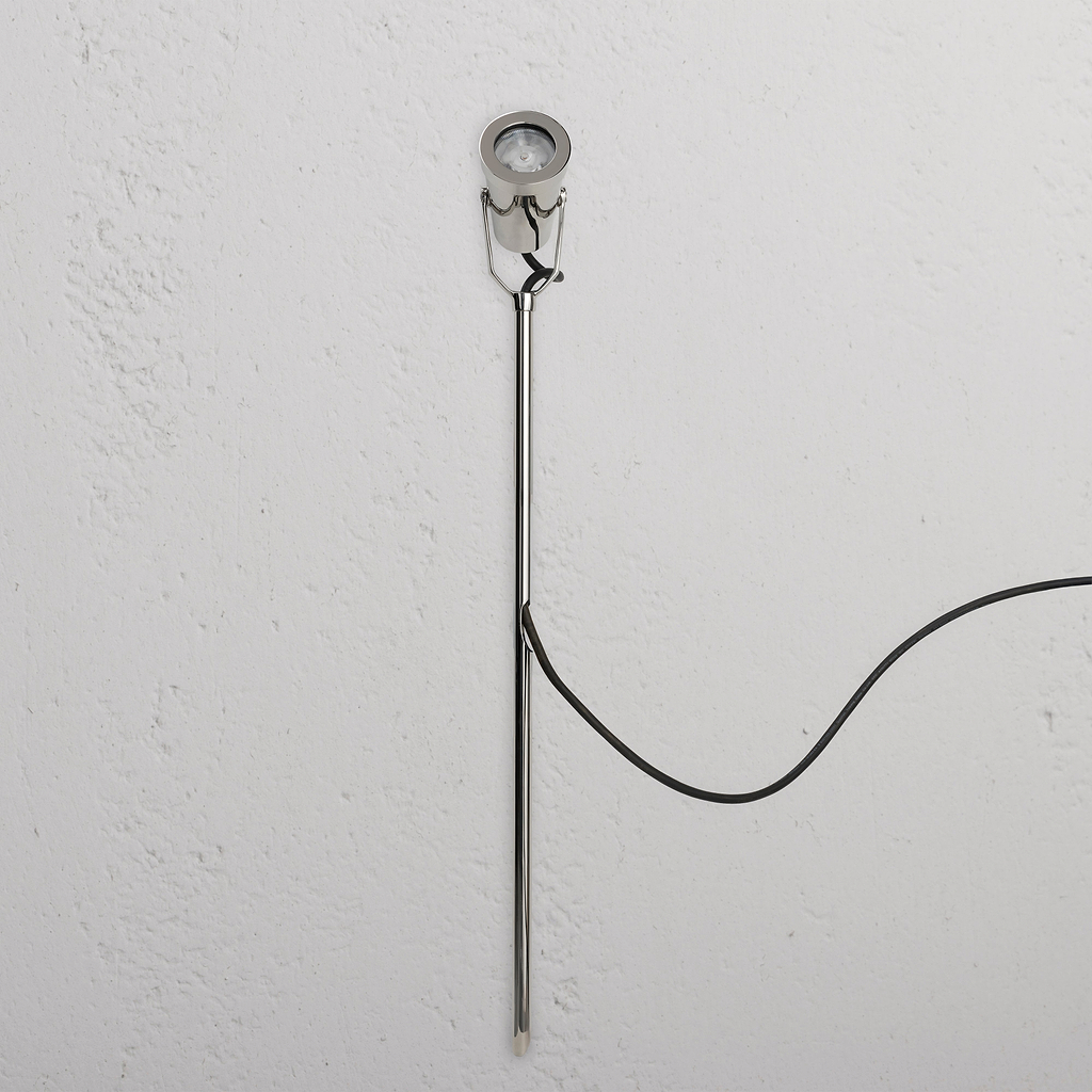 Cambridge Bodenstrahler Ã¢â‚¬â€œ Poliertes Nickel Outdoorstrahler mit rundem Leuchtkopf und schwarzem Kabel an weiÃƒÅ¸er Wand.