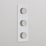 Vertikaler Dreifachrahmen mit 3x Dimmschalter, lackierbar, poliertes Nickel auf strukturiertem Hintergrund.