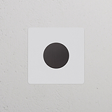 Einfachrahmen mit Mehrpunkt-Dimmerschalter, lackierbar in Weiß mit bronzefarbenem Dimmer, an weißer Wand.