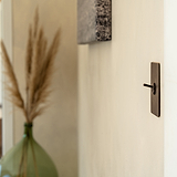 Kipphebelschalter – Bronze – an eine cremefarbene Wand montiert, grüne Glasvase im Hintergrund.