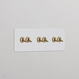 Dreifachrahmen mit 6 Kipphebelschaltern, lackierbar, in Antikmessing auf weißer Wand. Zur Individualisierung geeignet.