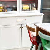 Bayswater Möbelknauf – Antikes Messing – an kleine weiße Schranktüren montiert mit einem waagerecht angebrachten Griff aus antikem Messing auf der darüber liegenden Schublade.