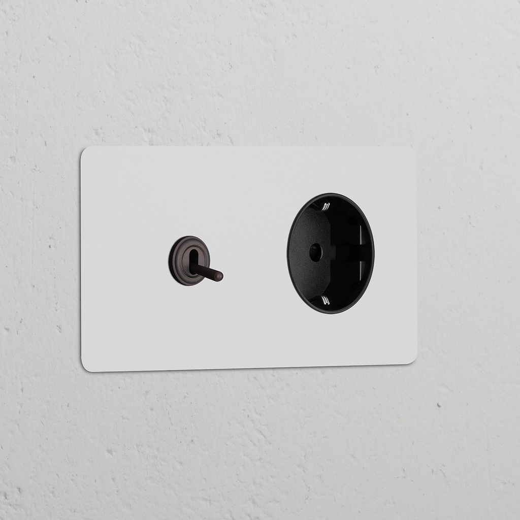 Zweifachrahmen mit Kipphebelschalter und Schuko-Steckdose Typ F auf weißem strukturiertem Wand, lackierbar in Bronze oder Schwarz.
