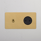 Kipphebel- und SchuKo-Modul in antikem Messing und Schwarz im runden Doppelrahmen mit Steckdosen auf weißer Strukturwand.