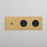 Eleganter Dreifachrahmen rund in antikem Messing mit 2 schwarzen Kipphebel & SchuKo-Modul-Schaltern an einer weißen Wand.