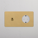 Antiker, runder Zweifachrahmen aus Messing und Weiß mit Kipphebel und SchuKo-Modul-Steckdosen vor einer weißen Wand.