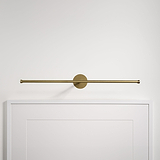 Lámpara de cuadro Taylor de 580 mm en latón antiguo, elegantemente colocada sobre un marco blanco en una pared sencilla.