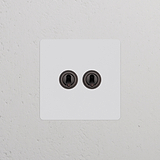 Interruptor de palanca doble elegante (pintable, bronce) en una pared blanca: tipo de marco individual.