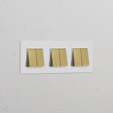 Marco triple con seis interruptores basculantes, pintable y de latón antiguo con inserto blanco, para control de iluminación.