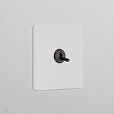 Interruptor de palanca pintable en bronce, para marco individual, montado en pared blanca.