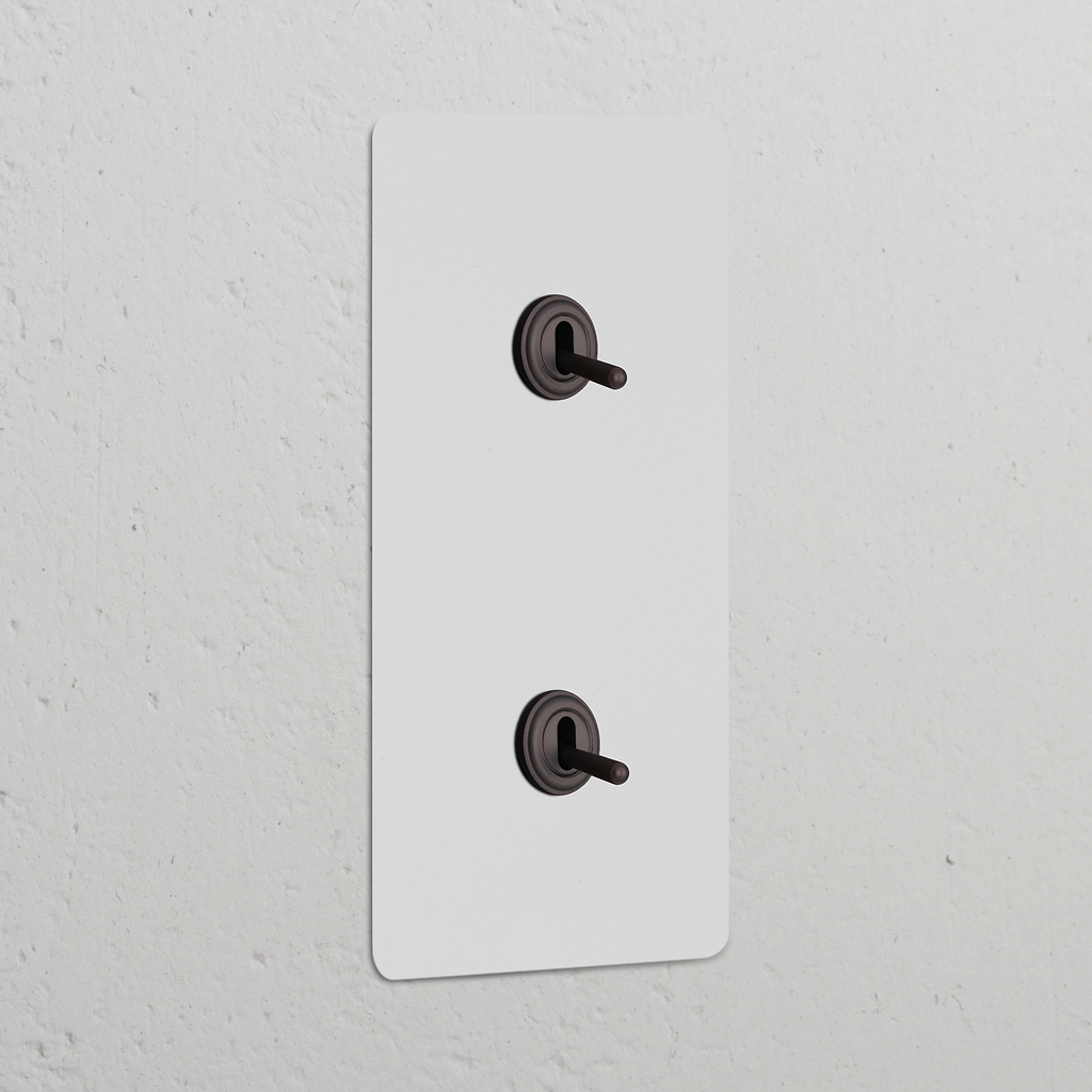 Interruptor conmutador de palanca x2 vertical en marco doble, pintable y bronce, ideal para control de luz.