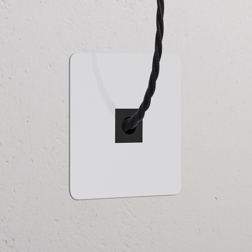 Salida de cable (marco individual) pintable con inserción negra, en placa blanca cuadrada sobre pared blanca texturizada.