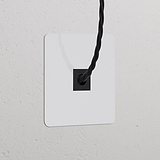 Salida de cable (marco individual) pintable con inserción negra, en placa blanca cuadrada sobre pared blanca texturizada.