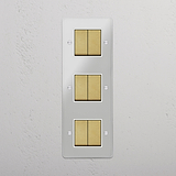 Solución superior de control de luces: Interruptor triple de balancín en latón antiguo y traslúcido con blanco con seis posiciones en diseño vertical sobre fondo blanco