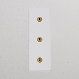 Interruptor triple vertical con marco de latón antiguo y pintable, apto para control de iluminación.