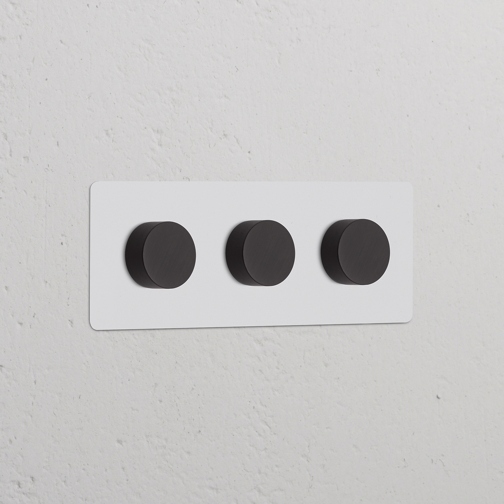 Interruptor regulador de luz multidireccional x3 en marco triple, pintable y bronce, montado en pared blanca.