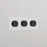 Interruptor regulador de luz multidireccional x3 en marco triple, pintable y bronce, montado en pared blanca.