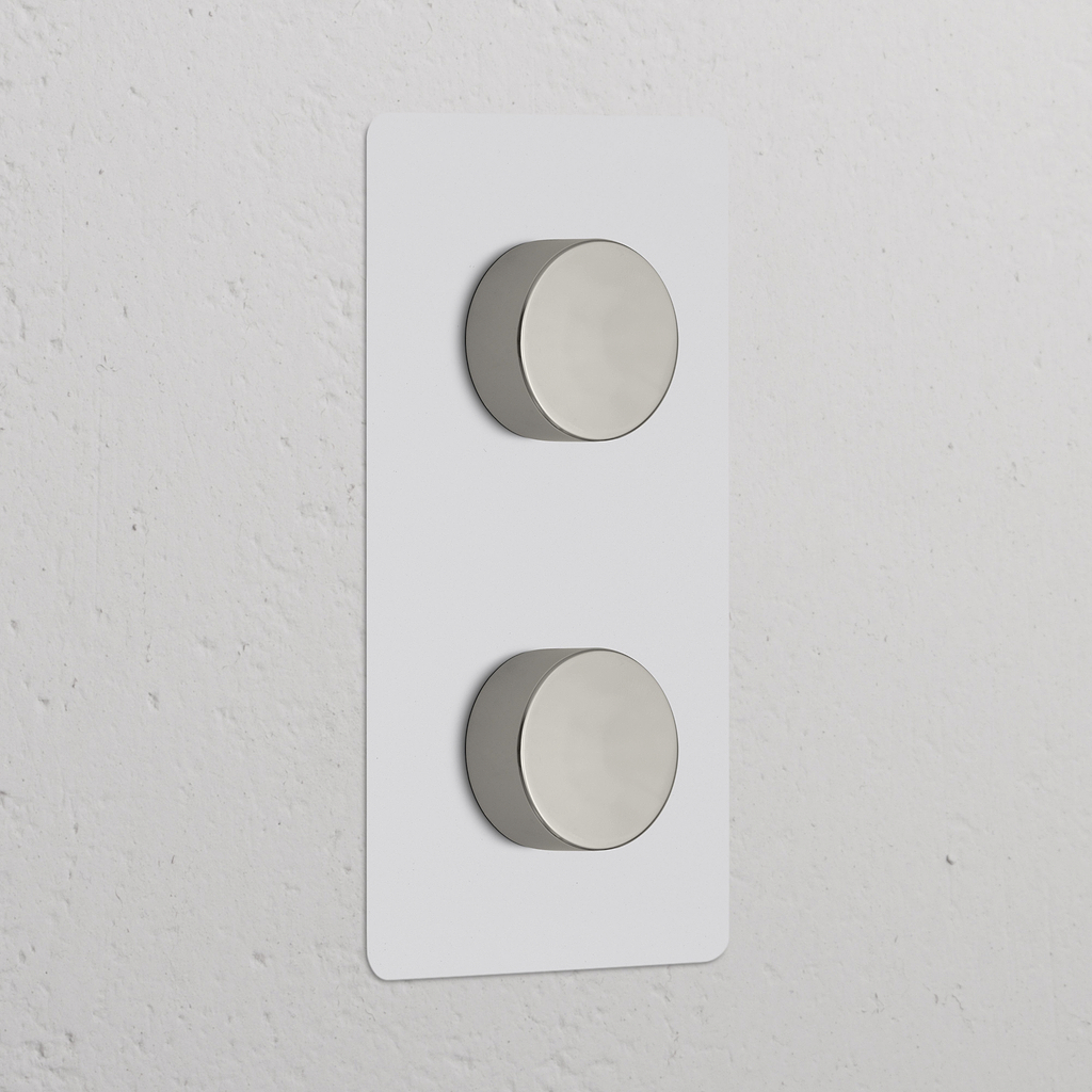 Interruptor regulador de luz vertical doble, pintable y níquel pulido, con dos perillas en marco rectangular.