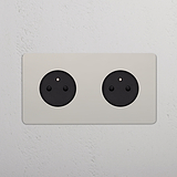 Prise murale double Type E (Plaque Double) en nickel poli avec insert noir sur paroi blanche.
