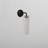 Claremont Petite Applique Murale Verre Cannelé avec luminaire en bronze, fixée au mur sur une surface texturée blanche.
